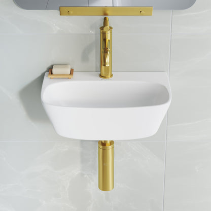 Small white wall-hung bathroom sink with gold wall-mounted faucet and matching gold drain pipe.