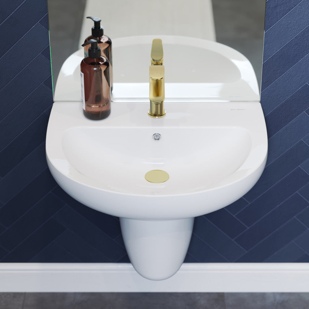 White ceramic wall-mount sink with gold faucet and amber soap dispenser on navy tile background.