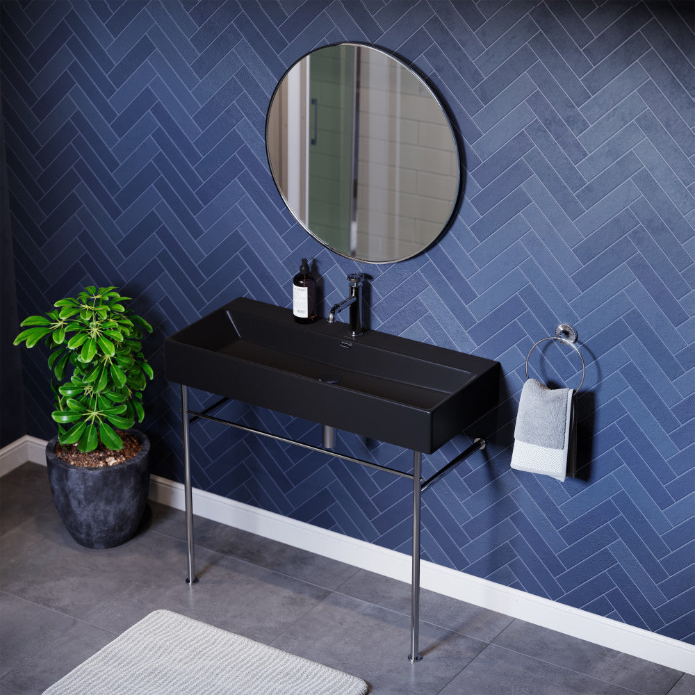 Matte black rectangular ceramic console sink with chrome legs and single-handle faucet against blue herringbone wall.