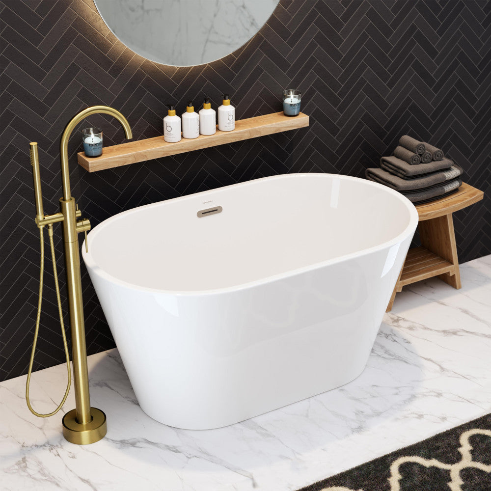 Freestanding white oval bathtub 48 inch with gold floor-mounted faucet on marble floor.