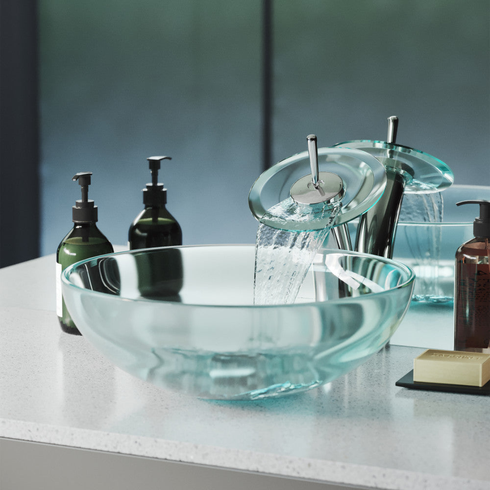 Clear round glass vessel sink with tall chrome single-handle faucet on white countertop.