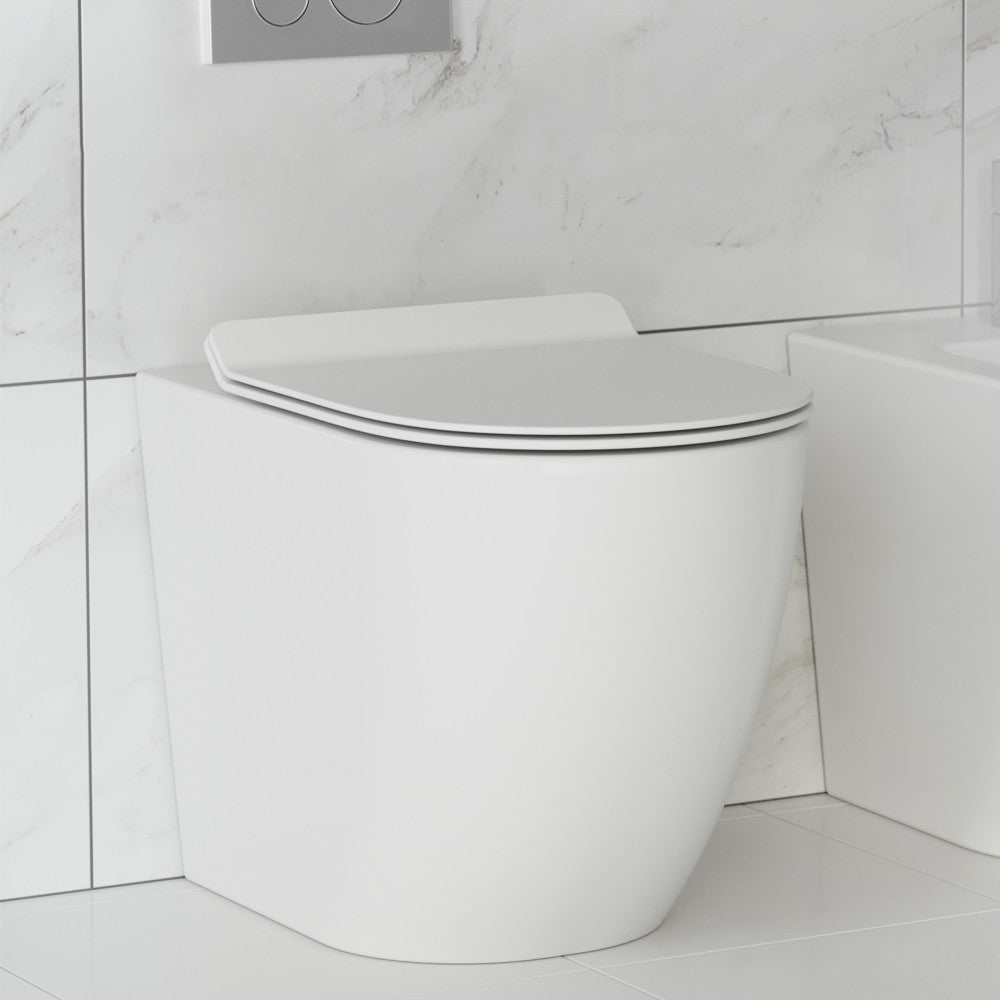 Elongated back-to-wall toilet with concealed tank and soft-close seat in white porcelain.