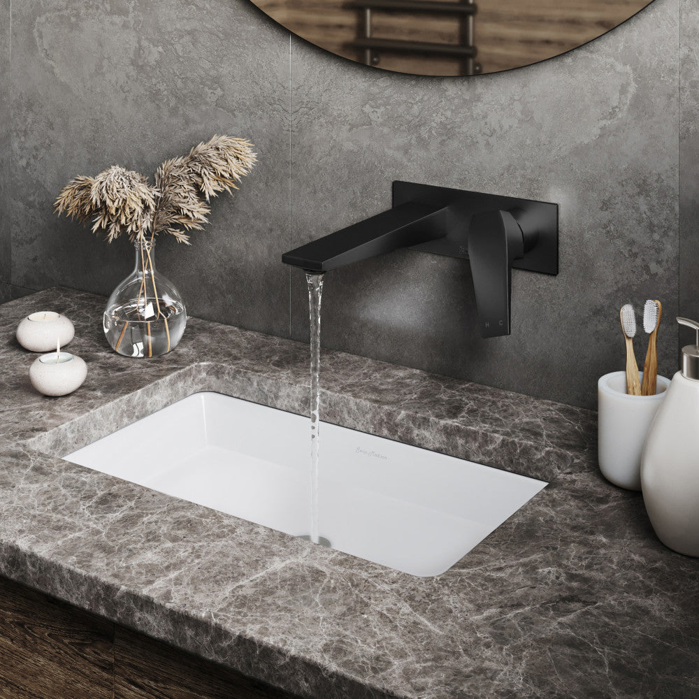 Wall-mount single-handle bathroom faucet in matte black with water flowing over rectangular undermount sink.